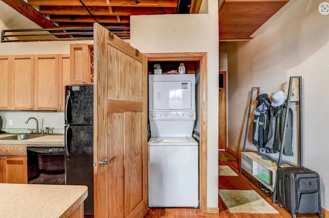 laundry room with wood finished floors, stacked washer and dryer, a sink, and laundry area