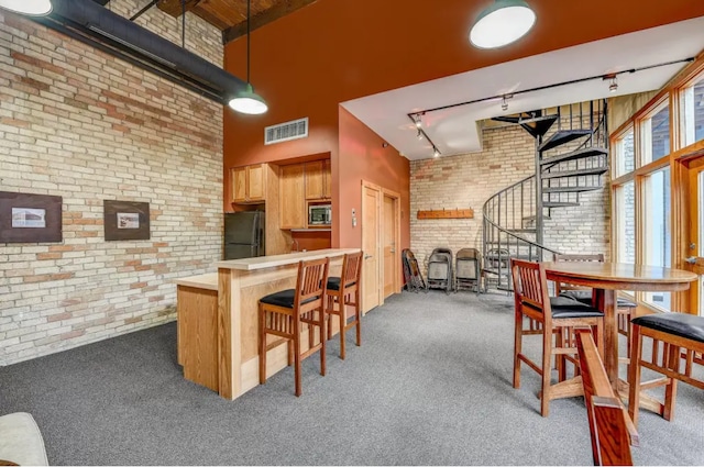 kitchen with visible vents, brick wall, freestanding refrigerator, carpet floors, and stainless steel microwave