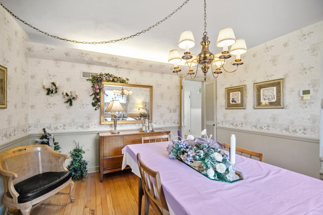 dining room with a chandelier, wallpapered walls, hardwood / wood-style flooring, and a wainscoted wall