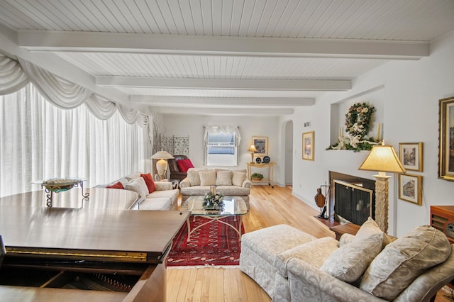 living area with arched walkways, wood-type flooring, beamed ceiling, and baseboards