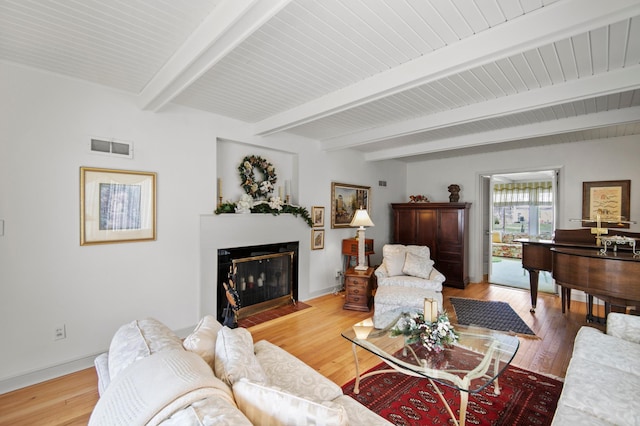 living area with a fireplace with flush hearth, beam ceiling, baseboards, and light wood-style flooring