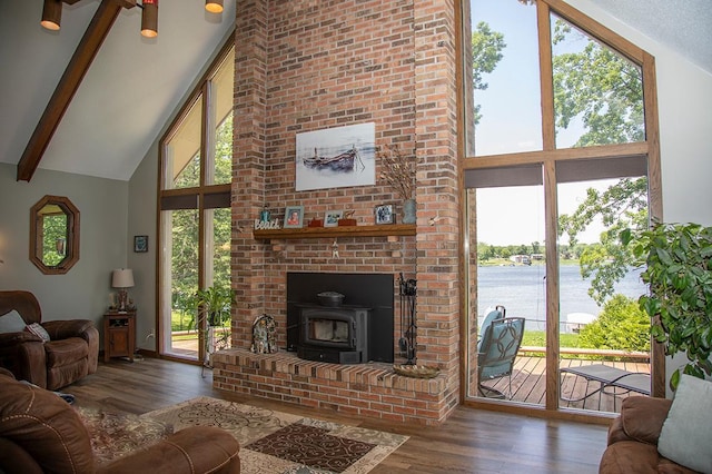 living area featuring a wood stove, high vaulted ceiling, a water view, wood finished floors, and beam ceiling