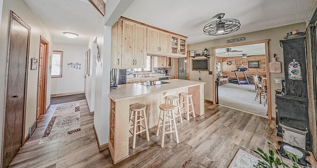 kitchen with plenty of natural light, a peninsula, a breakfast bar area, ceiling fan, and light wood finished floors