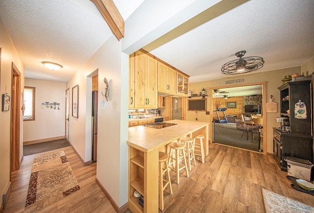 kitchen featuring a ceiling fan, a kitchen breakfast bar, light brown cabinetry, light wood-style floors, and a textured ceiling