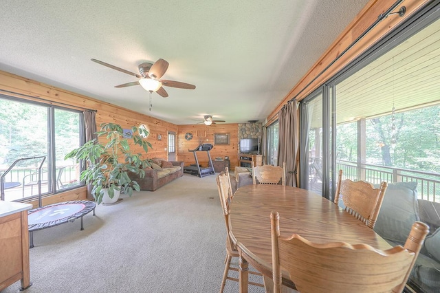 dining area featuring a textured ceiling, ceiling fan, wooden walls, and carpet