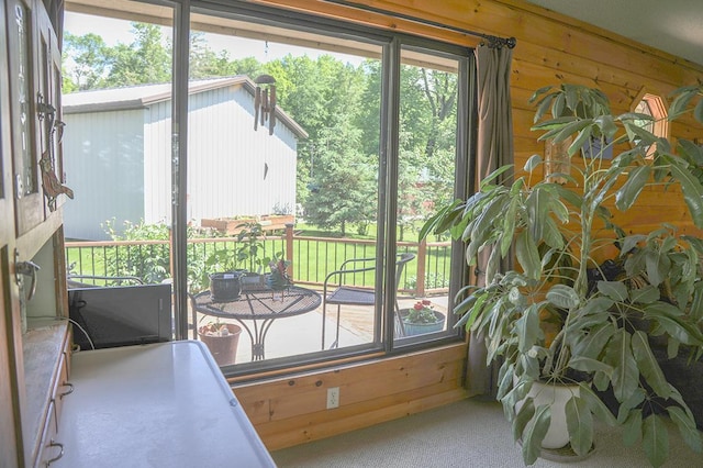 doorway to outside featuring wood walls, a wealth of natural light, and carpet
