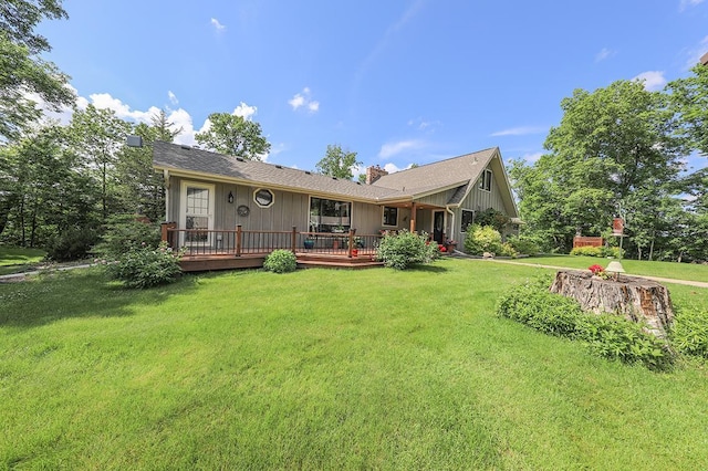back of property with a chimney, a wooden deck, and a lawn