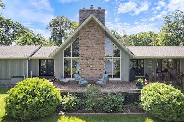 rear view of house featuring board and batten siding, roof with shingles, a deck, and a chimney