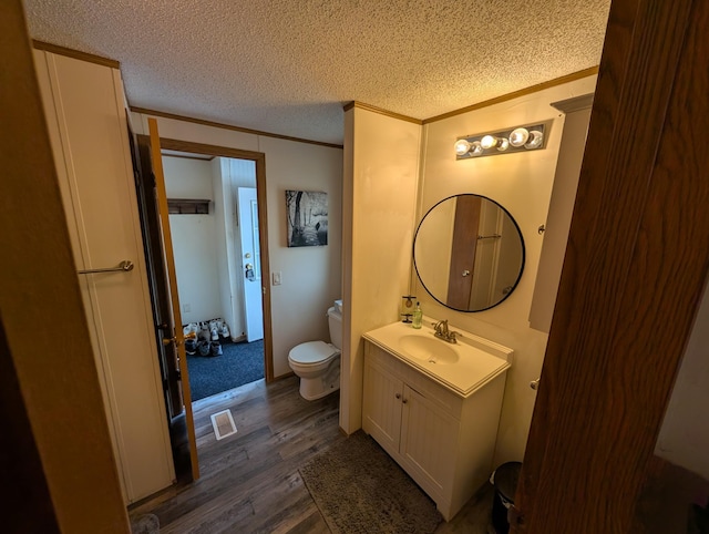 bathroom with toilet, a textured ceiling, crown molding, vanity, and wood finished floors