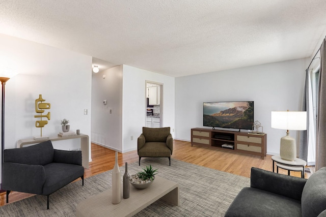 living area featuring light wood-type flooring, a textured ceiling, and baseboards