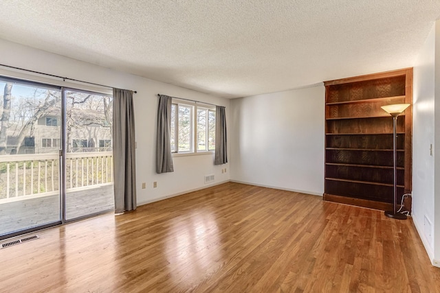 unfurnished living room featuring a textured ceiling, wood finished floors, and baseboards