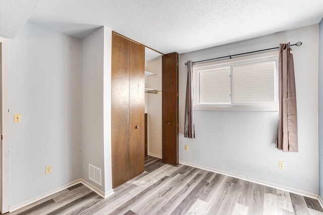 unfurnished bedroom featuring light wood-style flooring, a textured ceiling, a closet, and baseboards