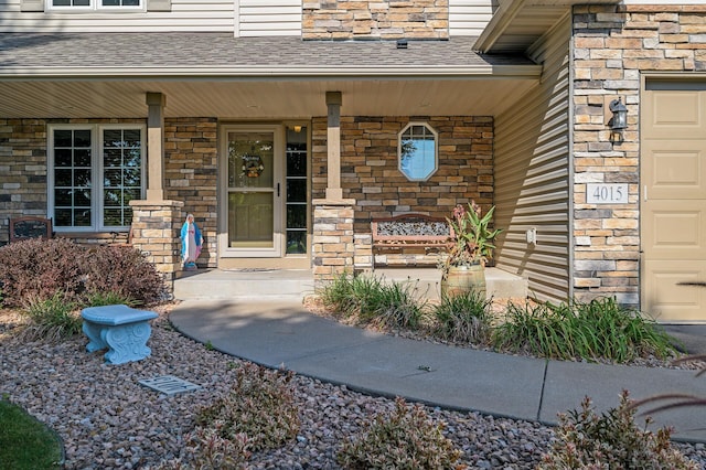 view of exterior entry with covered porch, a garage, roof with shingles, and stone siding