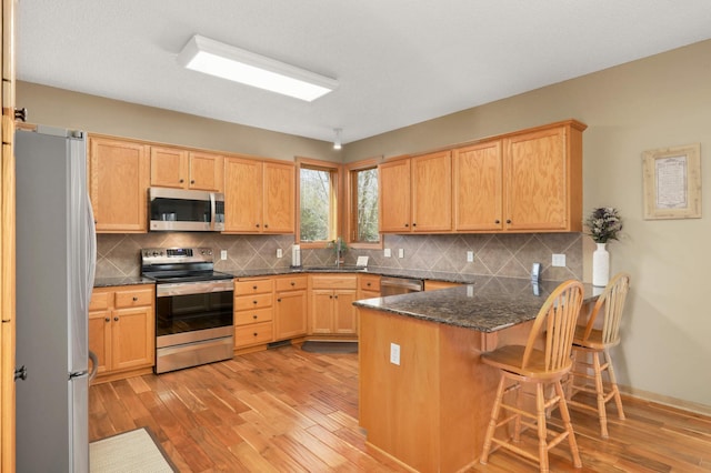 kitchen featuring tasteful backsplash, stainless steel appliances, a kitchen bar, light wood finished floors, and a peninsula