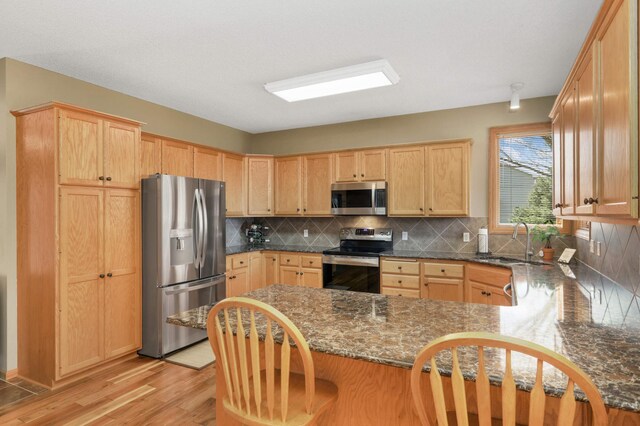 kitchen featuring a sink, light brown cabinets, tasteful backsplash, a peninsula, and appliances with stainless steel finishes