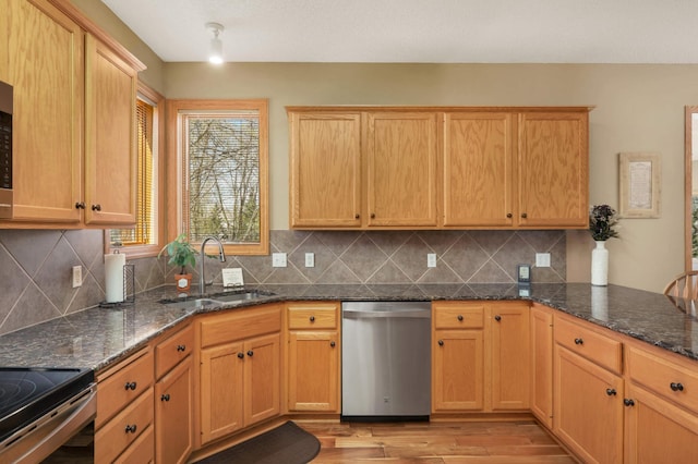 kitchen with stainless steel dishwasher, light wood-style flooring, dark stone counters, decorative backsplash, and a sink