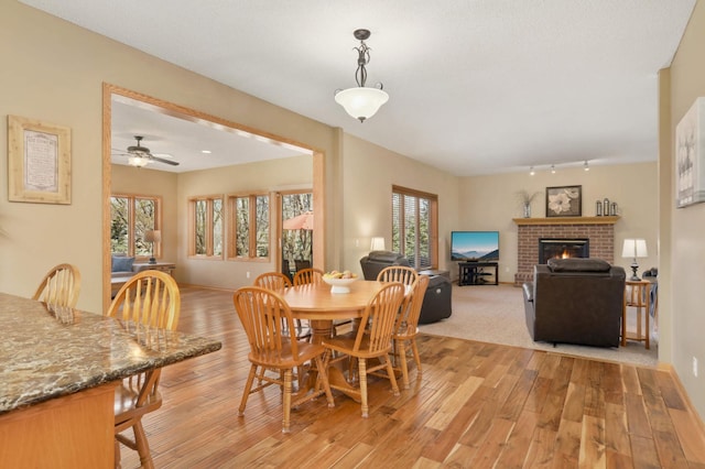 dining space with a brick fireplace, ceiling fan, light wood-type flooring, track lighting, and baseboards