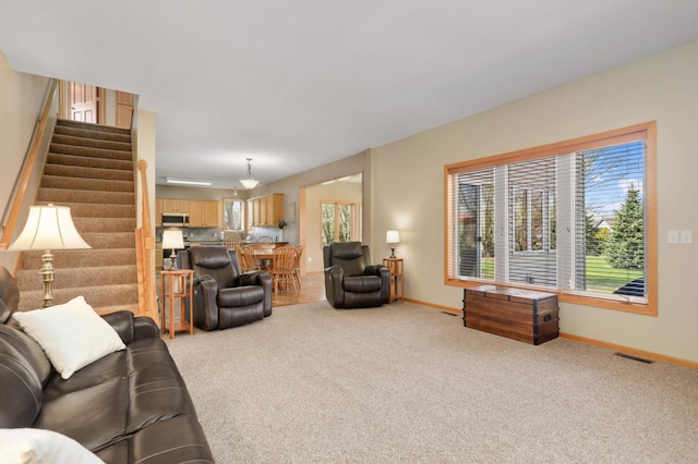 living room with visible vents, stairs, light colored carpet, and plenty of natural light
