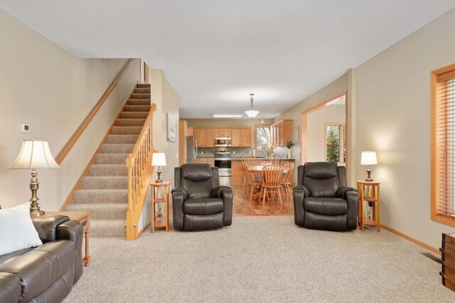 living area with baseboards, stairway, and light carpet