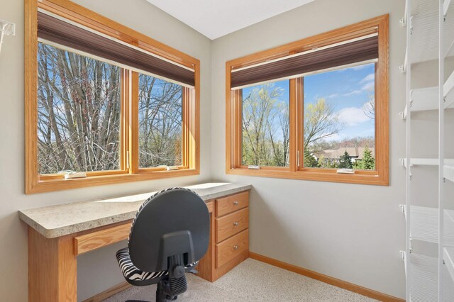 office space featuring baseboards, built in desk, and light carpet