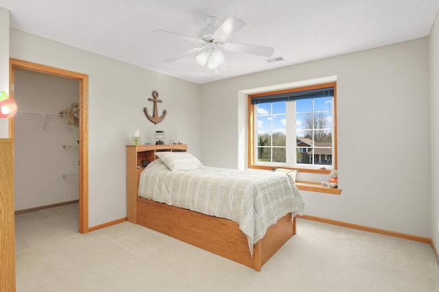 carpeted bedroom with a spacious closet, a closet, baseboards, visible vents, and a ceiling fan
