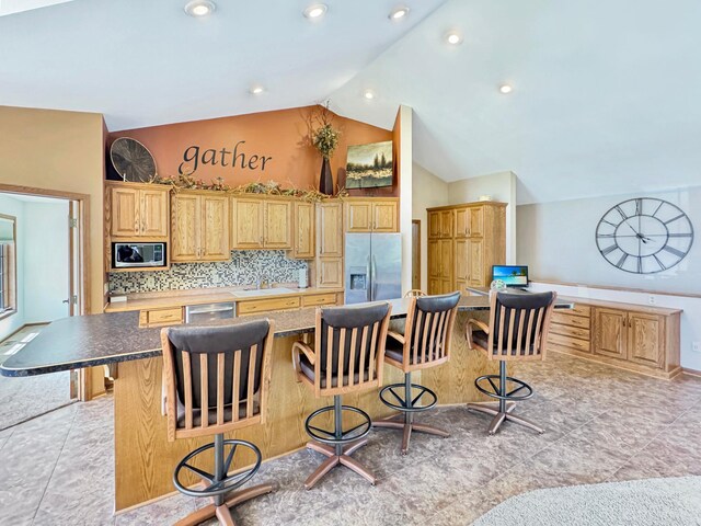 kitchen featuring stainless steel appliances, a kitchen breakfast bar, a sink, tasteful backsplash, and vaulted ceiling