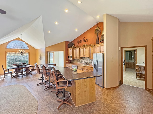 kitchen featuring high vaulted ceiling, dark countertops, light tile patterned flooring, a breakfast bar area, and stainless steel appliances