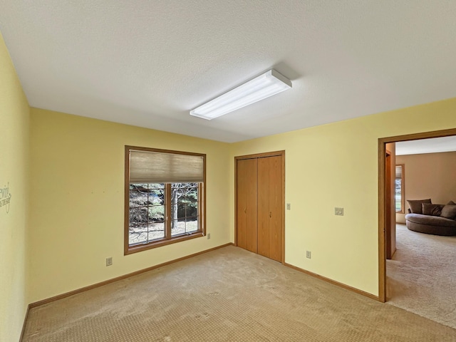 interior space featuring baseboards, a closet, light colored carpet, and multiple windows