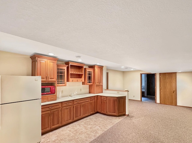 kitchen with a peninsula, a sink, freestanding refrigerator, glass insert cabinets, and light countertops