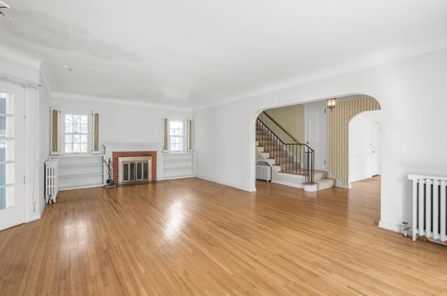 unfurnished living room with radiator heating unit, arched walkways, and light wood-style floors