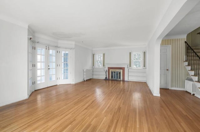 unfurnished living room with baseboards, stairway, light wood-style flooring, radiator heating unit, and a brick fireplace