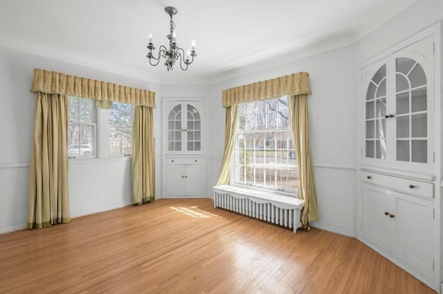 unfurnished dining area with radiator heating unit, light wood-type flooring, and a chandelier