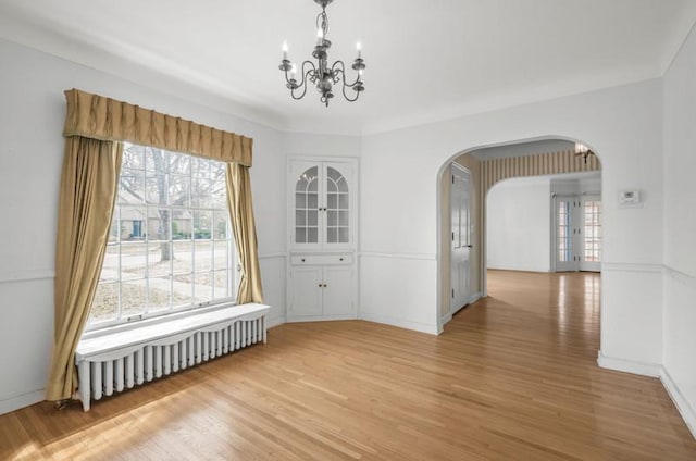 unfurnished dining area featuring a chandelier, arched walkways, radiator, and light wood-type flooring