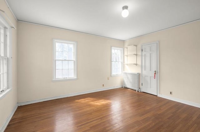 empty room with baseboards, crown molding, radiator, and wood finished floors
