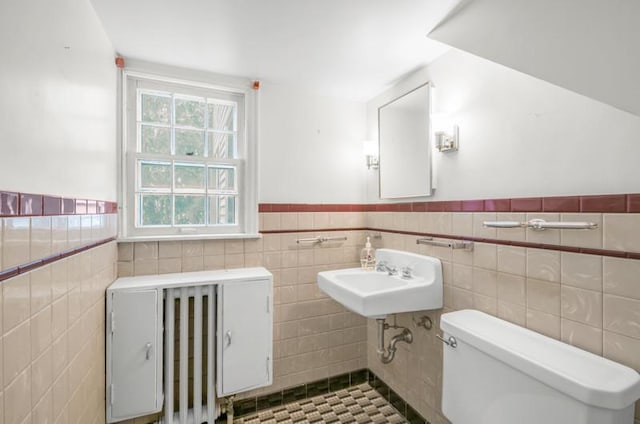 bathroom featuring toilet, a sink, wainscoting, and tile walls