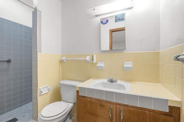 full bath with vanity, toilet, wainscoting, tile walls, and a tile shower
