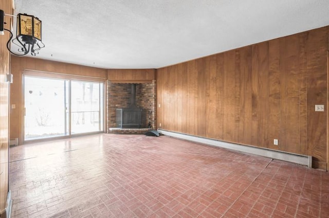 unfurnished living room with a wood stove, wooden walls, baseboard heating, and brick patterned floor
