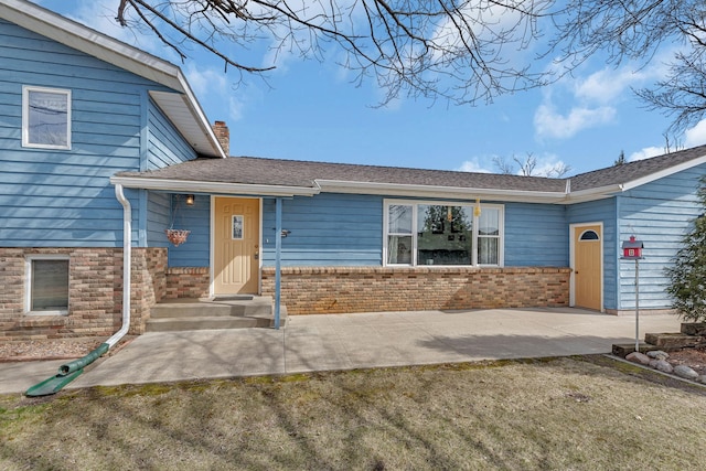 tri-level home with a chimney, brick siding, a front yard, and roof with shingles