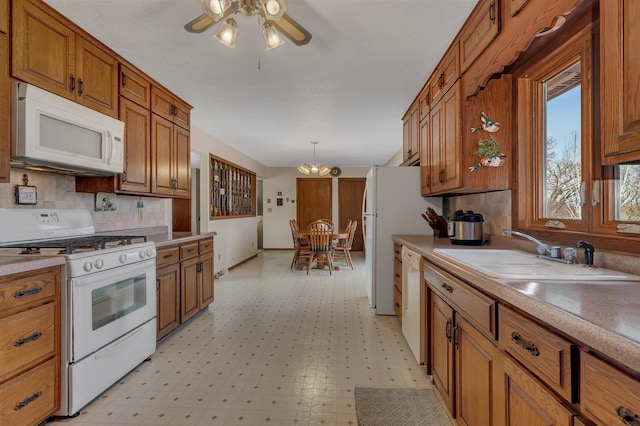 kitchen with a sink, ceiling fan with notable chandelier, brown cabinetry, white appliances, and light countertops