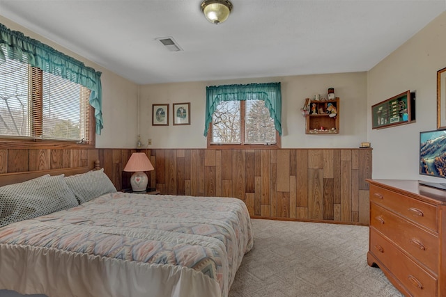 carpeted bedroom with wood walls, a wainscoted wall, visible vents, and multiple windows