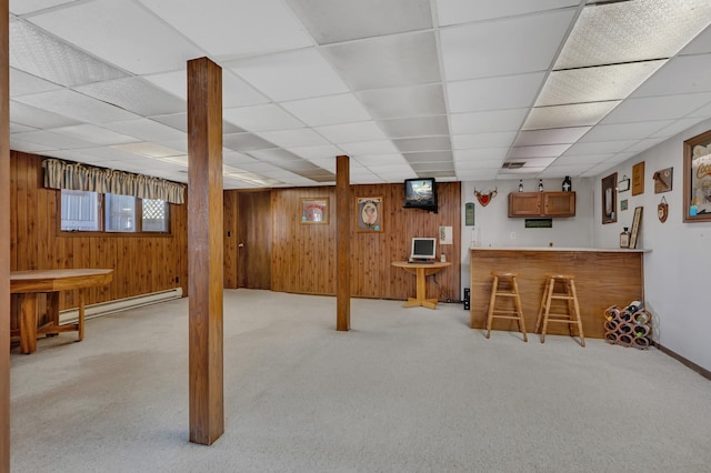 below grade area featuring wood walls, a baseboard heating unit, indoor wet bar, light carpet, and baseboards
