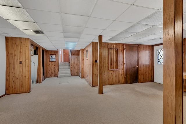 basement featuring wood walls, carpet, stairs, and a drop ceiling