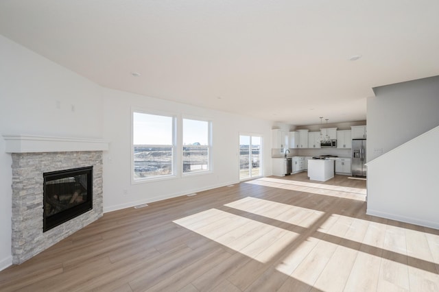 unfurnished living room with baseboards, visible vents, light wood finished floors, and a fireplace