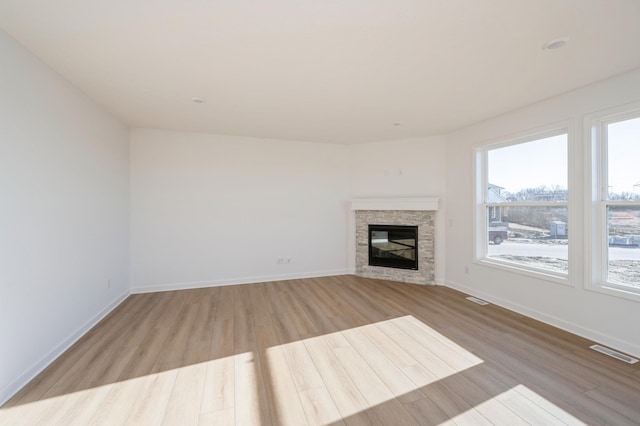 unfurnished living room with wood finished floors, visible vents, a stone fireplace, and a healthy amount of sunlight