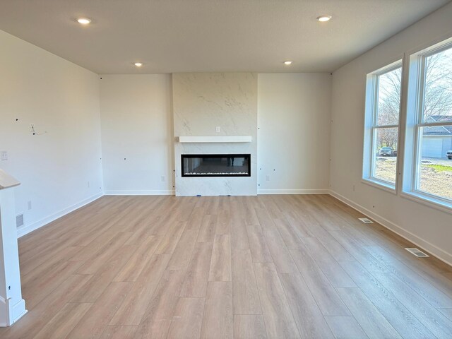 unfurnished living room with recessed lighting, plenty of natural light, baseboards, a glass covered fireplace, and light wood-style flooring