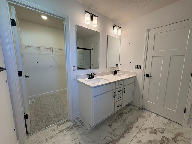 bathroom with double vanity, marble finish floor, a sink, and a walk in closet