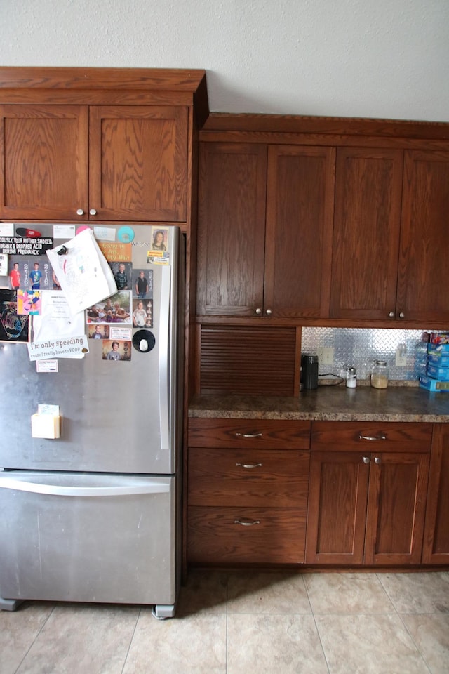 kitchen featuring dark countertops, freestanding refrigerator, brown cabinetry, and light tile patterned flooring