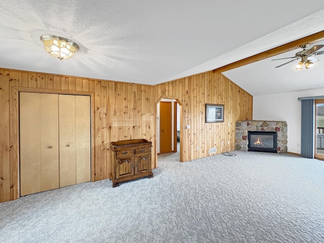 living area featuring vaulted ceiling, a stone fireplace, carpet flooring, and wood walls