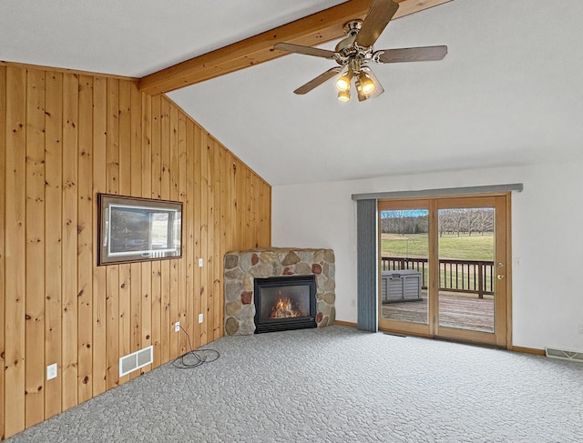 carpeted living area featuring wooden walls, a stone fireplace, visible vents, and lofted ceiling with beams