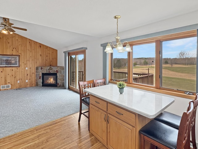 kitchen featuring light wood-type flooring, vaulted ceiling, visible vents, wood walls, and a fireplace